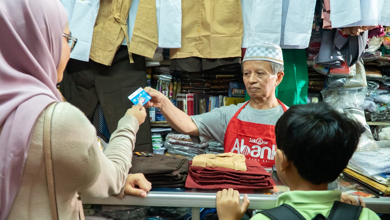 Pedagang pakaian yang juga Agen JakOne Abank tengah melayani pembeli yang bertransaksi dengan Kartu Jakarta Pintar Plus, di Pasar Santa, Jakarta Selatan, Selasa (30/4/2024). dok. ist.. Dukung Pelaku UMKM, Bank DKI Gencarkan Layanan JakOne Abank